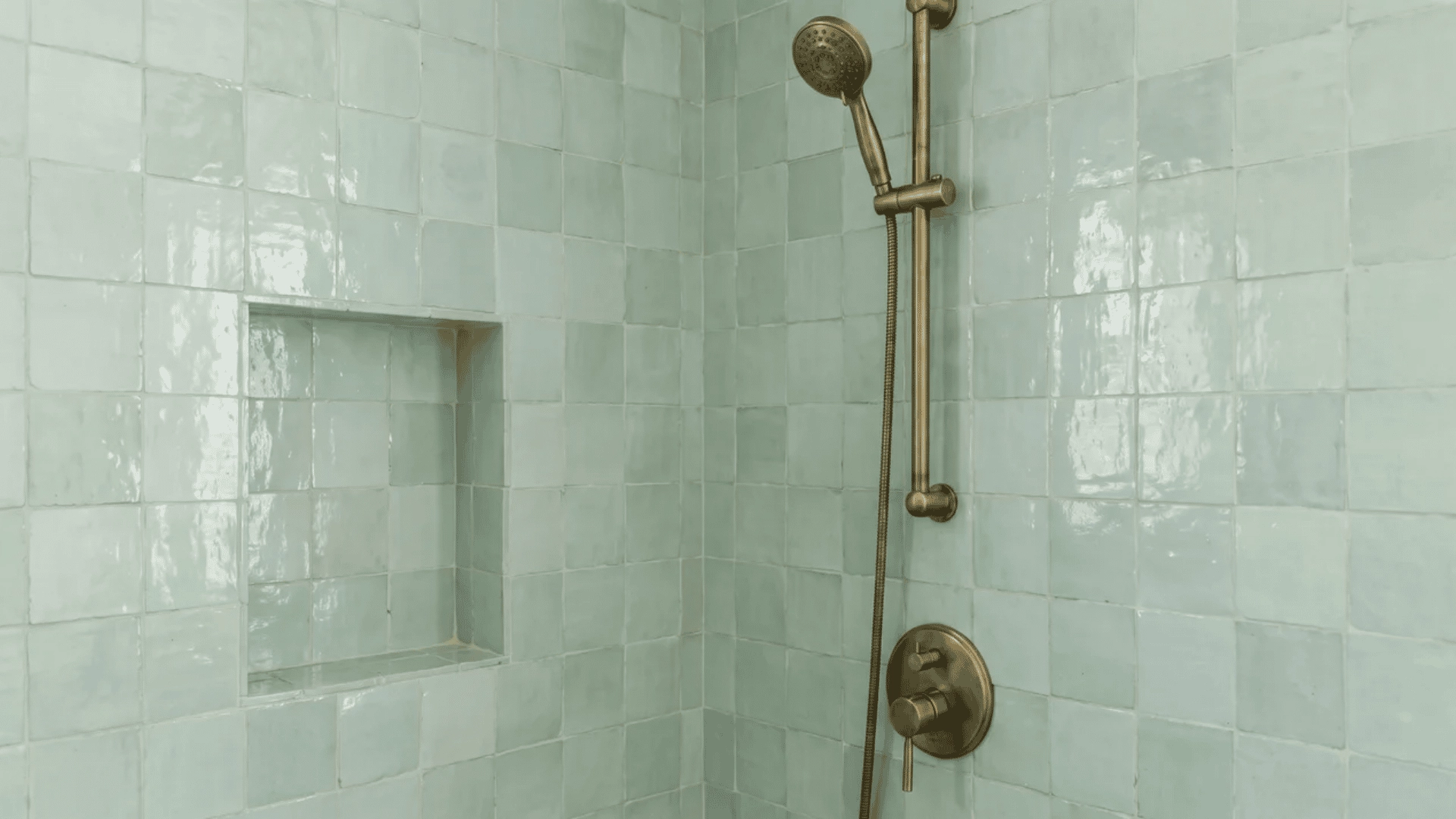 Pale seafoam zellige tile shower surround with brass fixtures