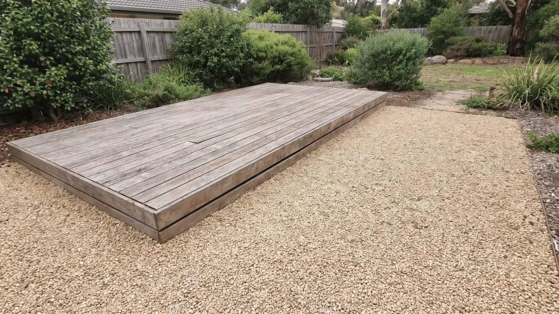 Small wood deck platform beside an adjoining pea gravel zone in a residential yard