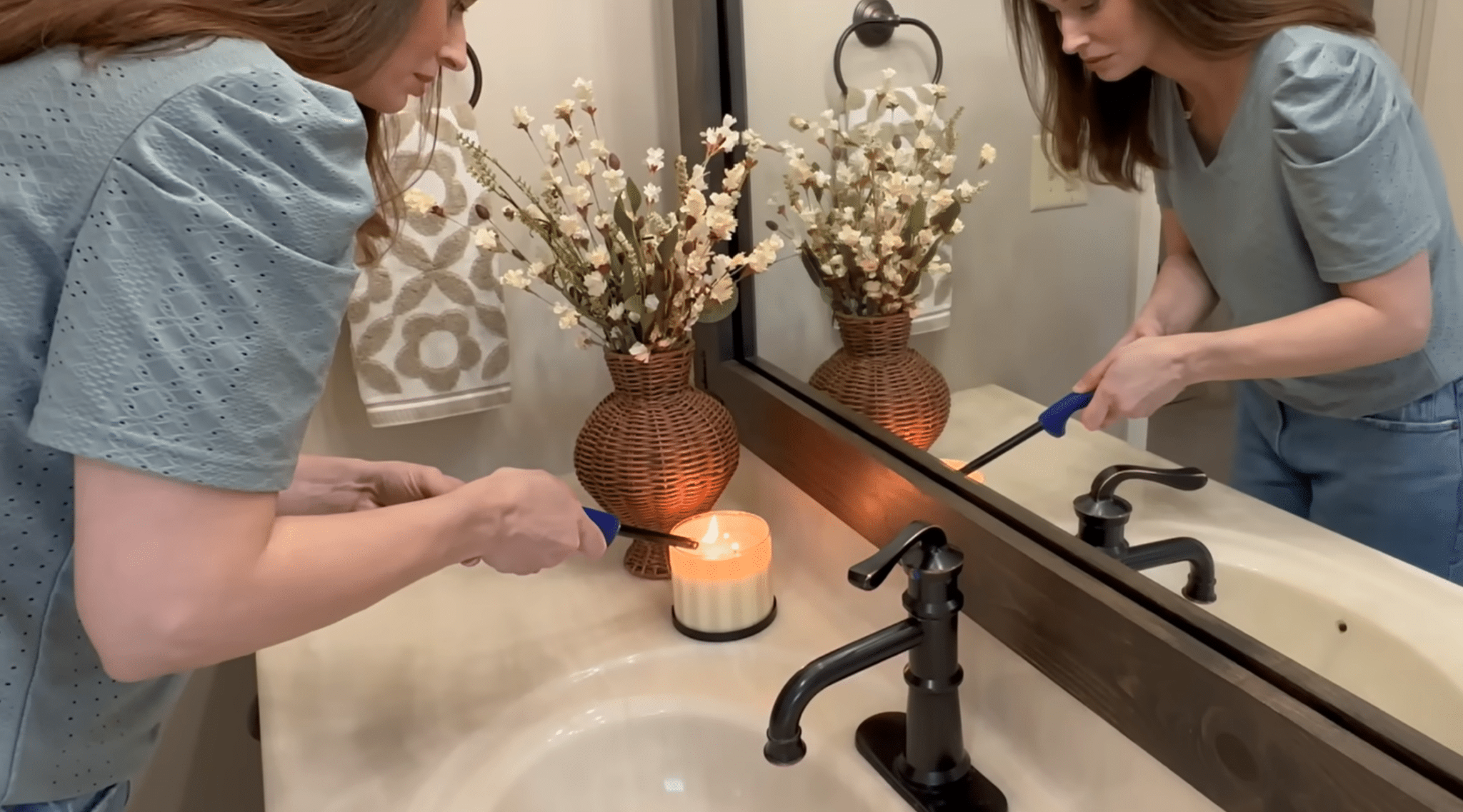Person adding a candle and floral vase to a bathroom vanity for a warm, decorative refresh.