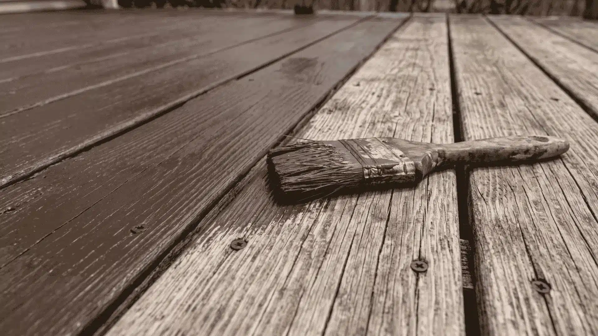 Solid-color stain being applied across weathered wooden deck boards