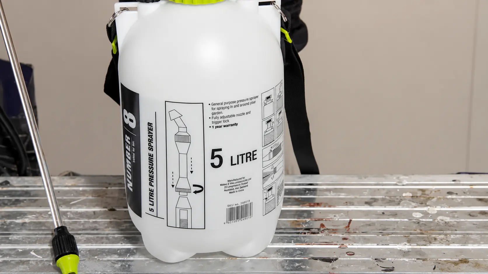 White 5-liter pressure sprayer with wand placed on a workbench for wallpaper glue removal preparation