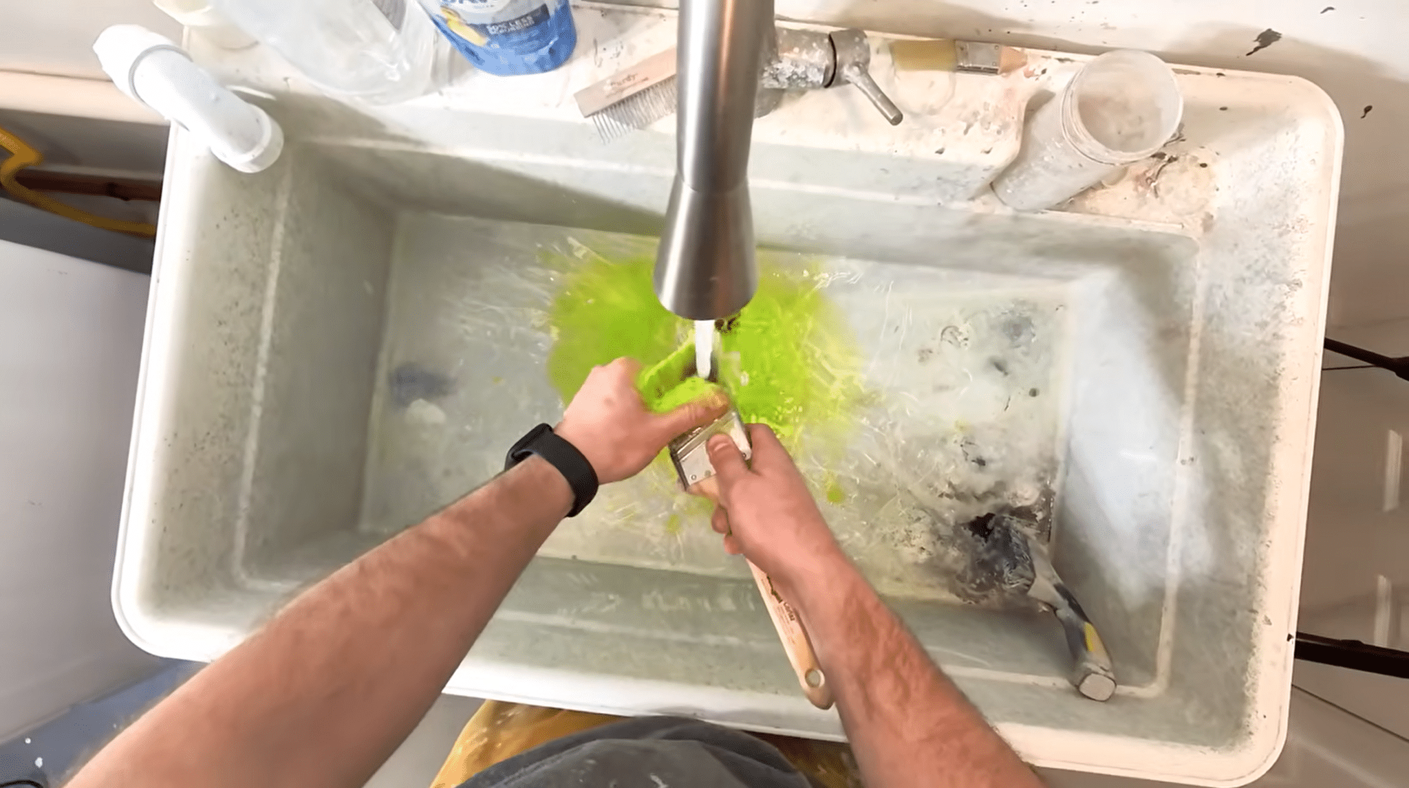 Paint brush being rinsed under running water while the bristles are cleaned in a sink.