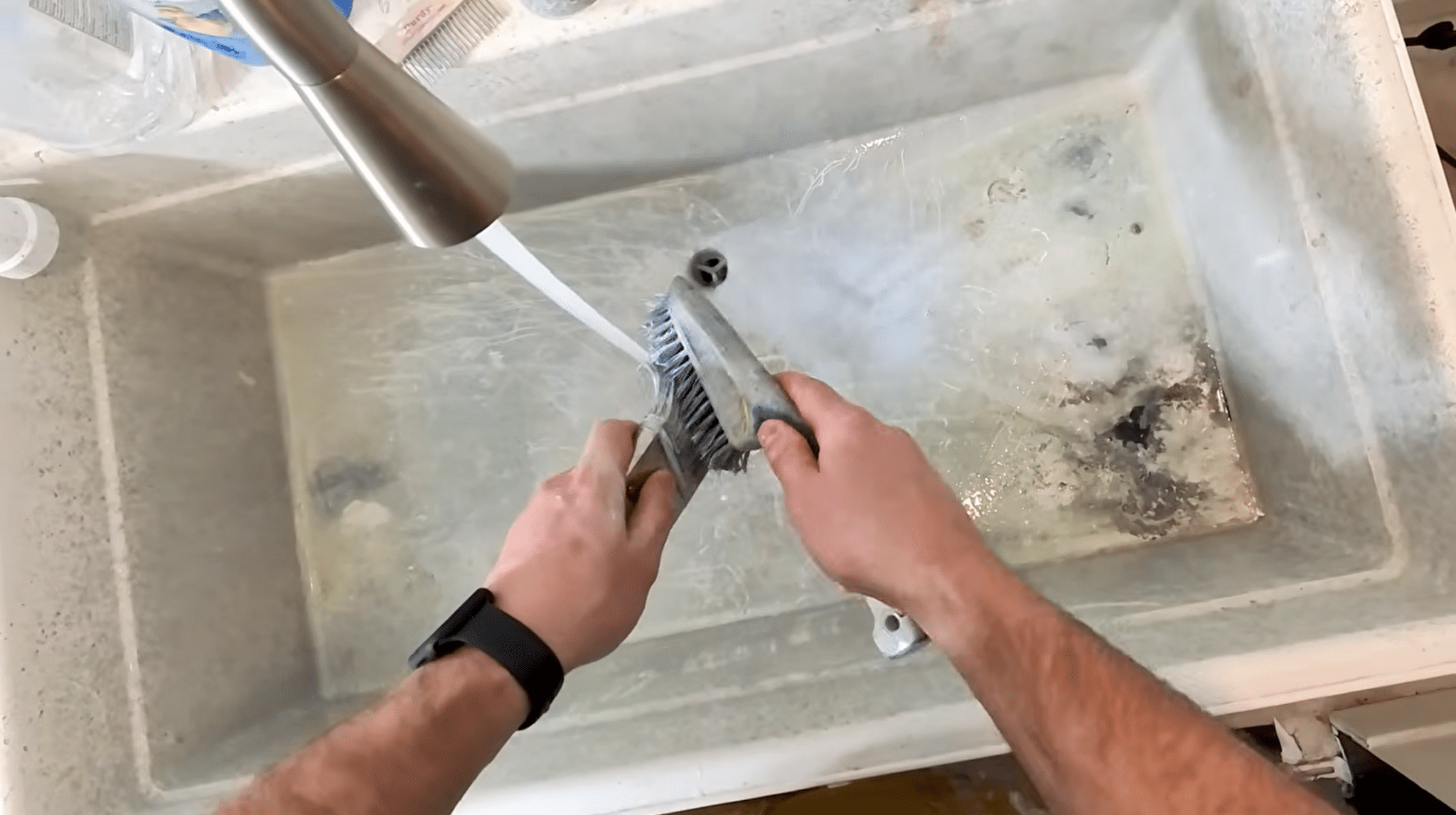 Cleaning dried paint from a brush near the ferrule using a wire brush under running water.