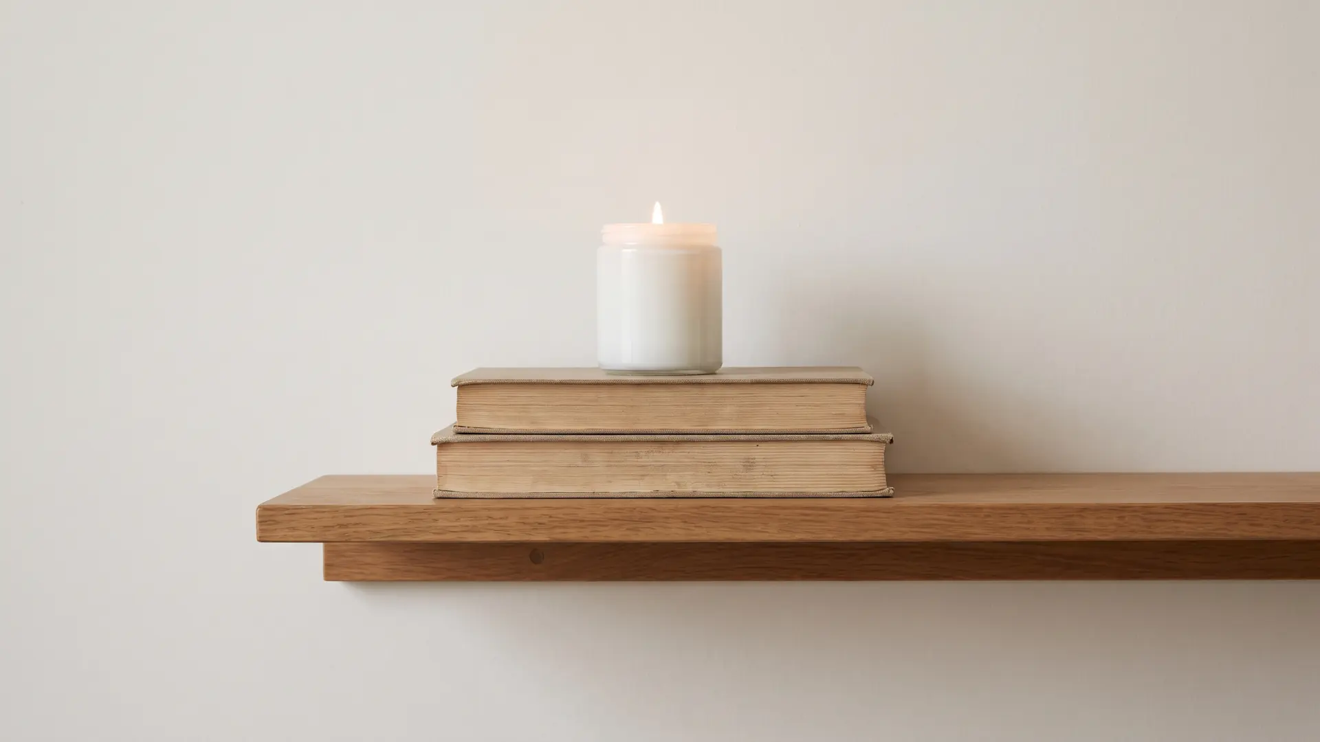 Stacked books on a shelf topped with a small candle