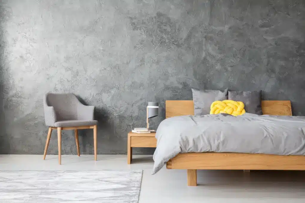 Modern bedroom with wooden bed, grey bedding, and yellow cushion against textured grey wall