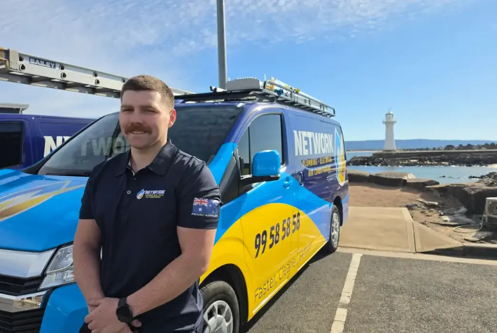 Man in uniform standing beside company van with lighthouse in the background