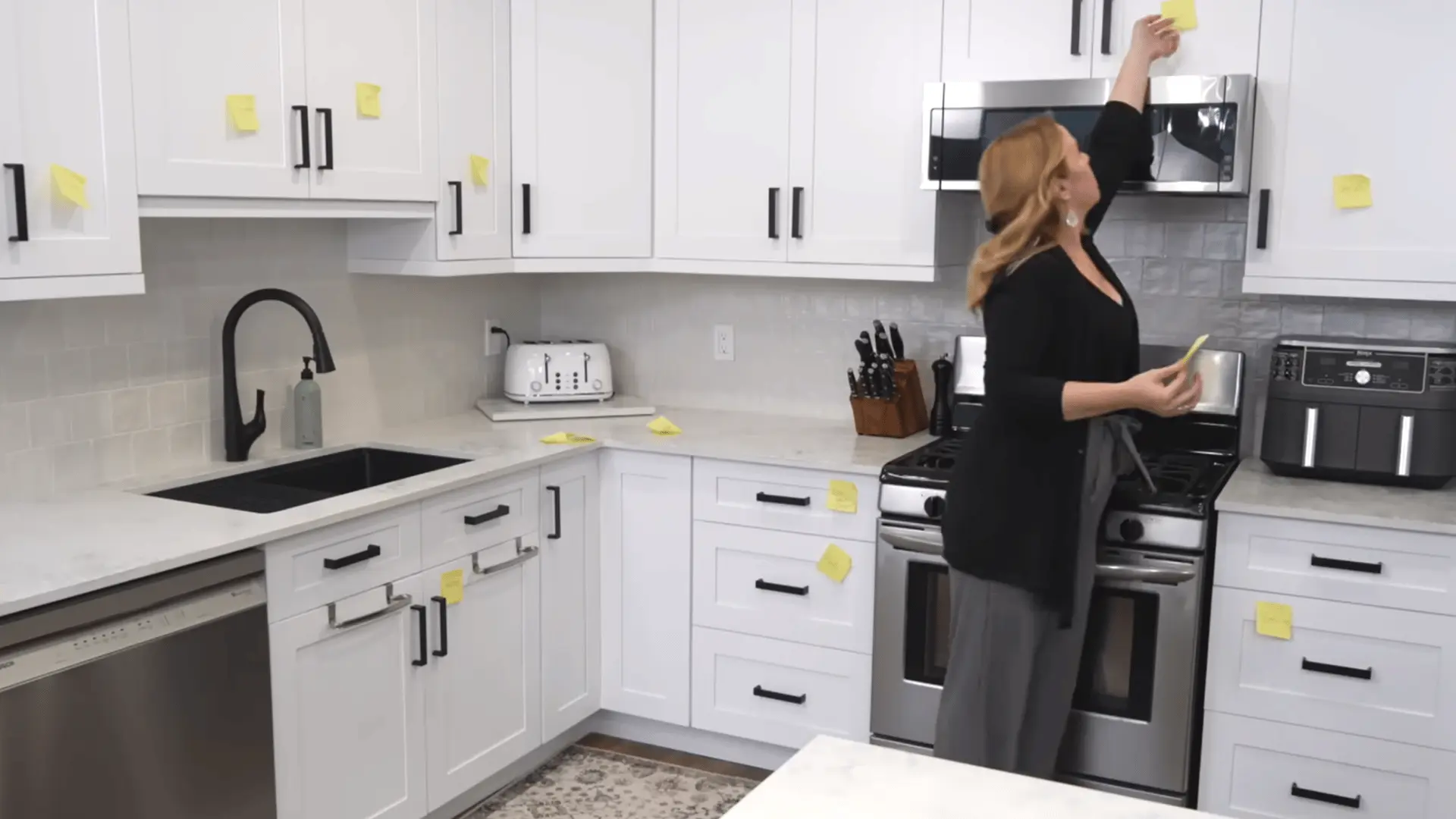 Woman removes sticky notes from kitchen cabinets after finishing the new storage zones.