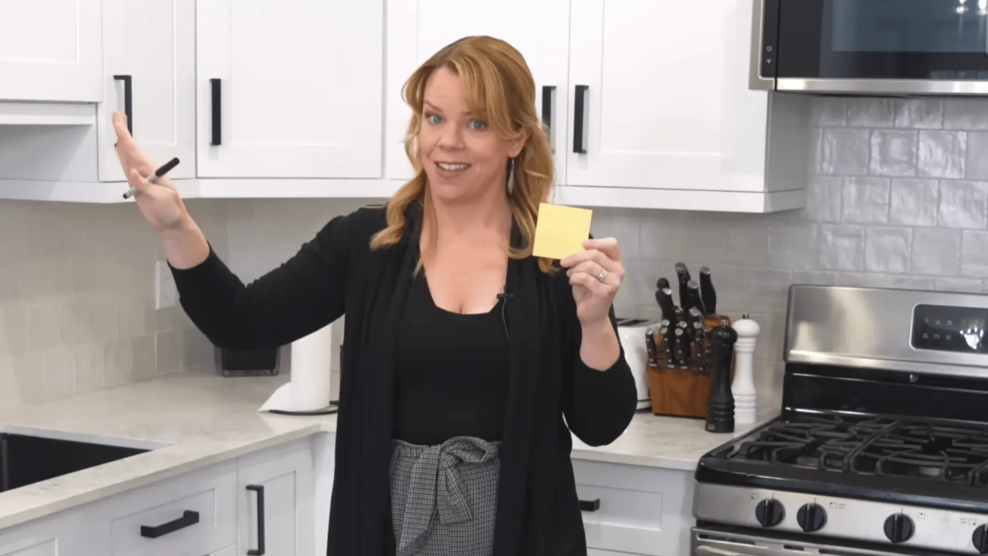Woman uses sticky notes and a marker to plan storage zones in a white kitchen.