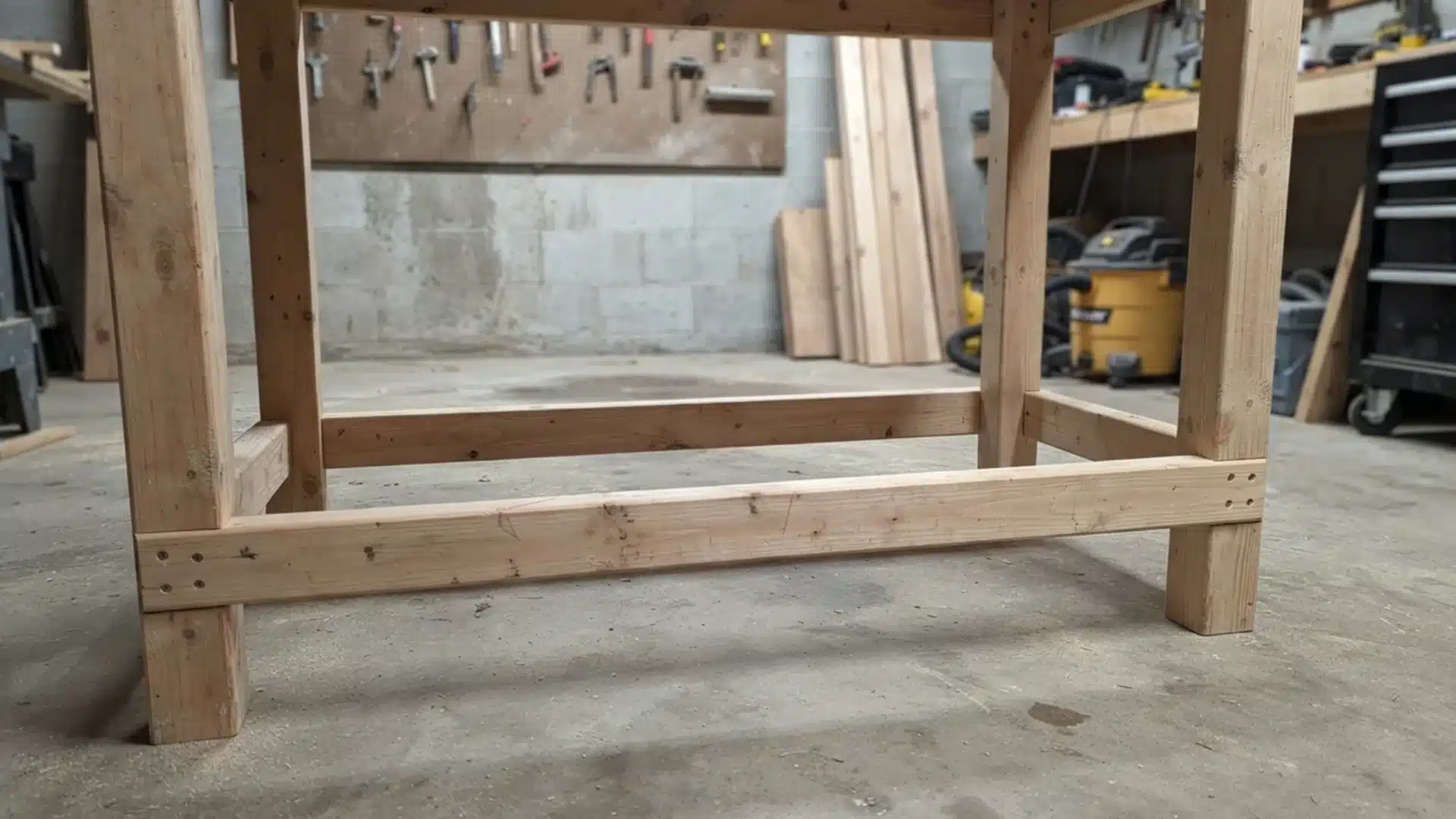 Lower support stretchers attached to four wooden legs of a sturdy DIY workbench frame.