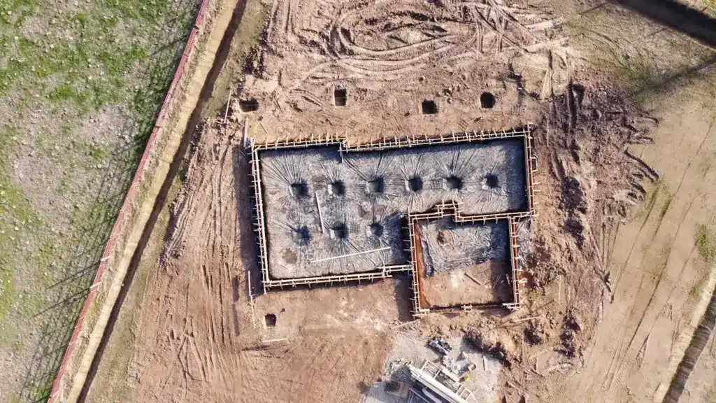 Aerial view of construction site with concrete foundation framed on dirt terrain
