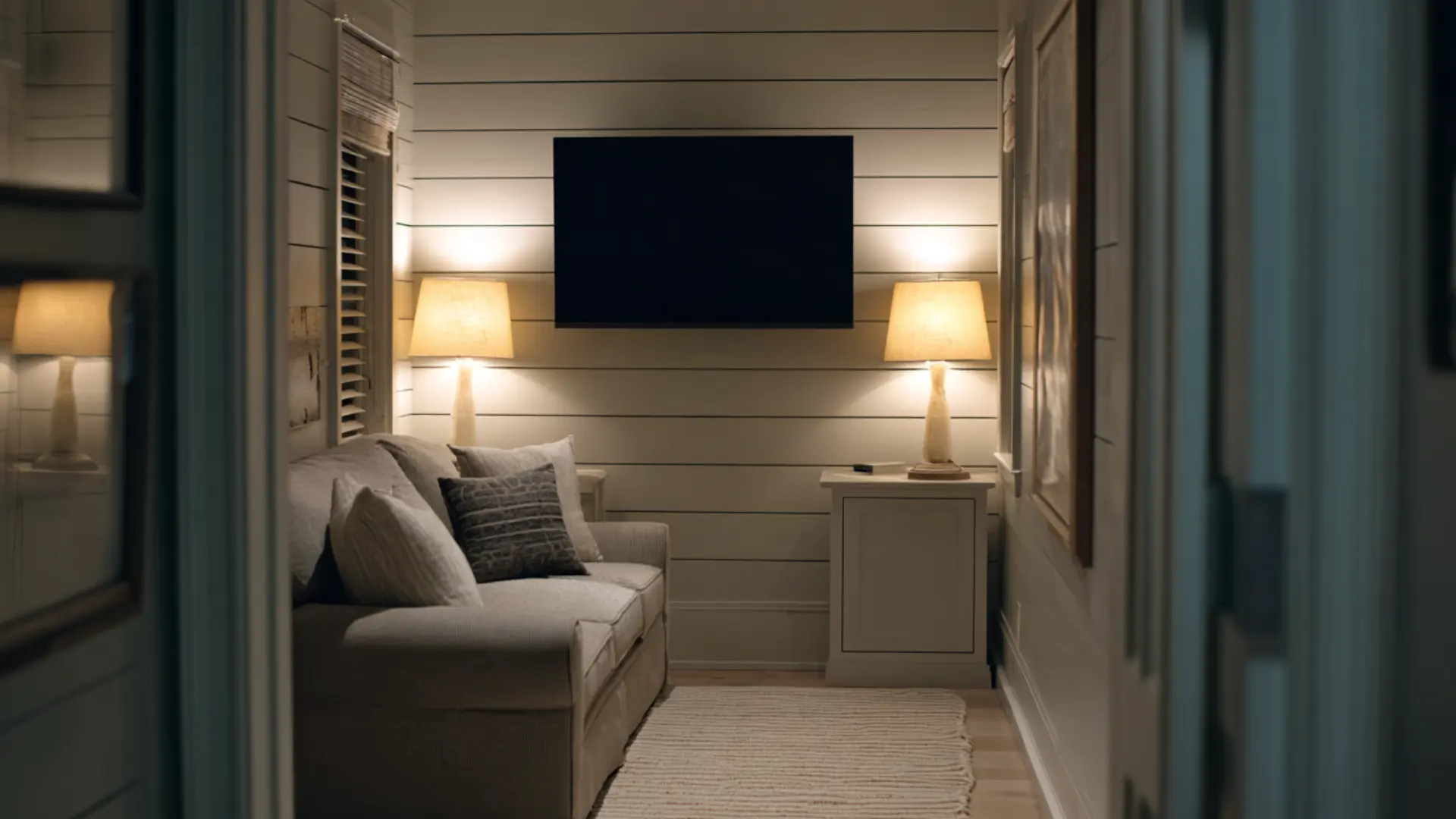 narrow den media room with a wall mounted flat screen on shiplap a two seat sofa two table lamps and a rug
