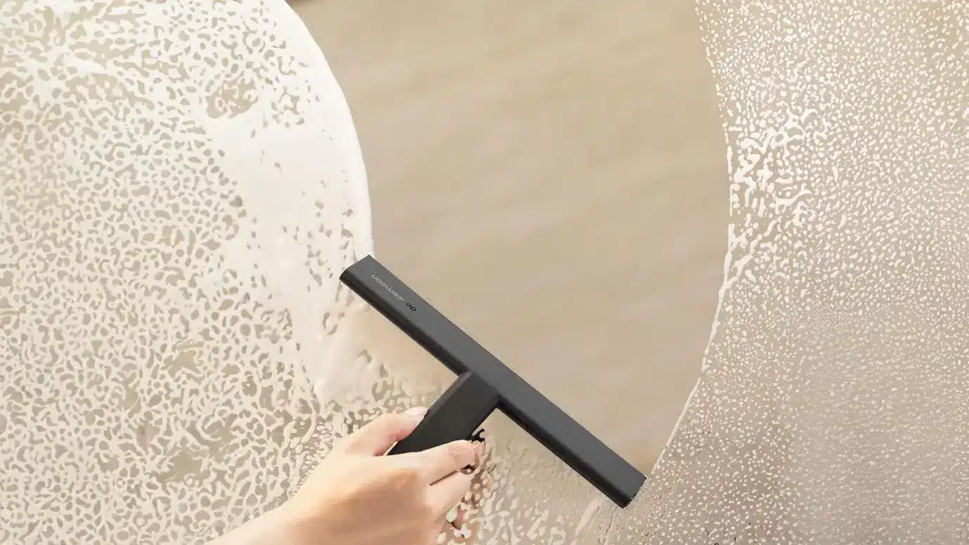 Hand using a black squeegee to clean soapy glass indoors